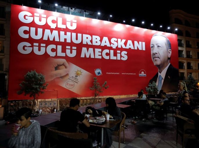 People sit in a restaurant terrace as a pre-election poster depicting Turkish President Tayyip Erdogan reads