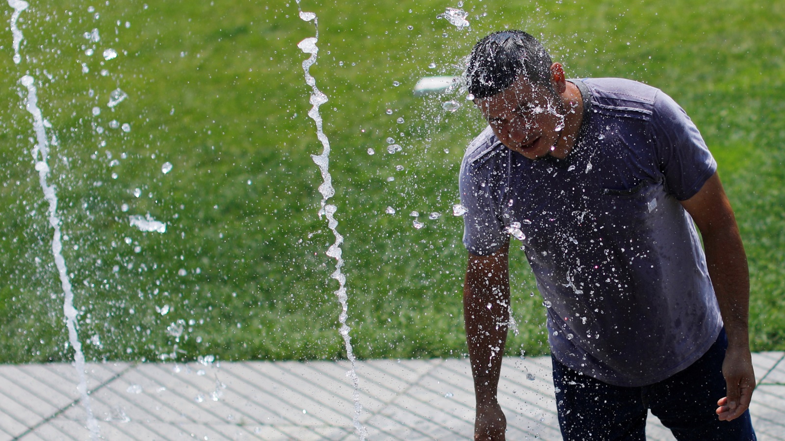 مواطن أميركي يلجأ إلى نافورة مياه لتخفيف وطأة درجة الحرارة غير المسبوقة (رويترز)