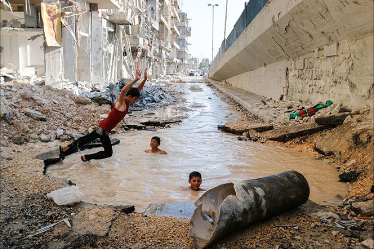 A boy dives into a crater filled with water in the Al-Shaar neighborhood. The crater was made by a barrel bomb. (Hosam Katan)