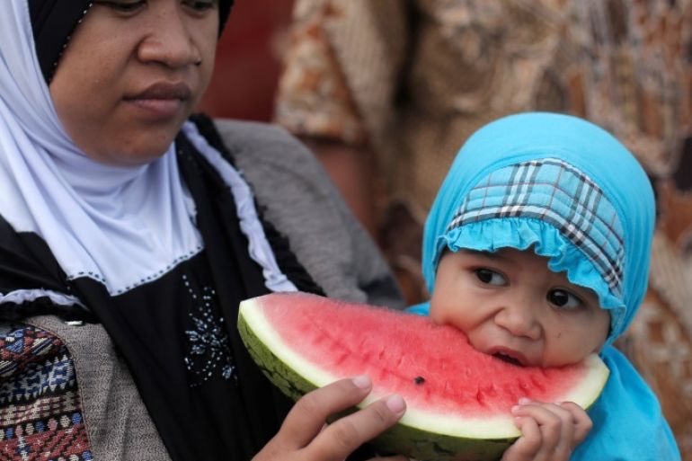 A mother holds her child eating a watermelon during prayers for the Muslim holiday of Eid Al-Adha at Sunda Kelapa port in Jakarta, Indonesia September 1, 2017. REUTERS/Beawiharta