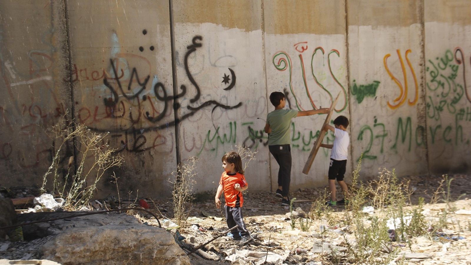يستمر الأطفال باللعب خلف الجدار وحدهم والخوف حولهم من كل جانب بفعل ممارسات الاحتلال وملاحقته (الجزيرة)