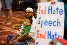 Attendees sit next to a poster as speakers from different faiths speak at an interfaith rally titled
