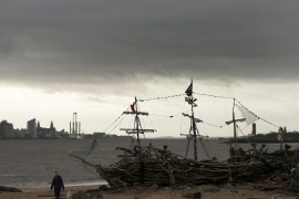 A women walks her dog under a dark sky past the Black Pearl driftwood pirate ship on New Brighton beach near Wallasey in Britain January 26, 2016. REUTERS/Phil Noble