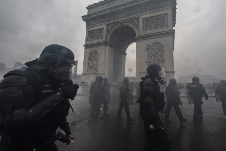 PARIS, FRANCE - DECEMBER 01: Teargas surrounds riot police as they clash with protesters during a 'Yellow Vest' demonstration near the Arc de Triomphe on December 1, 2018 in Paris, France. The third 'Yellow Vest' (gilets jaunes) rally in Paris over increased fuel taxes and leadership in the government today caused over 150 arrests in the city with reports of injuries to protesters and security forces from violence that irrupted from the clashes. (Photo by Veronique de Viguerie/Getty Images)