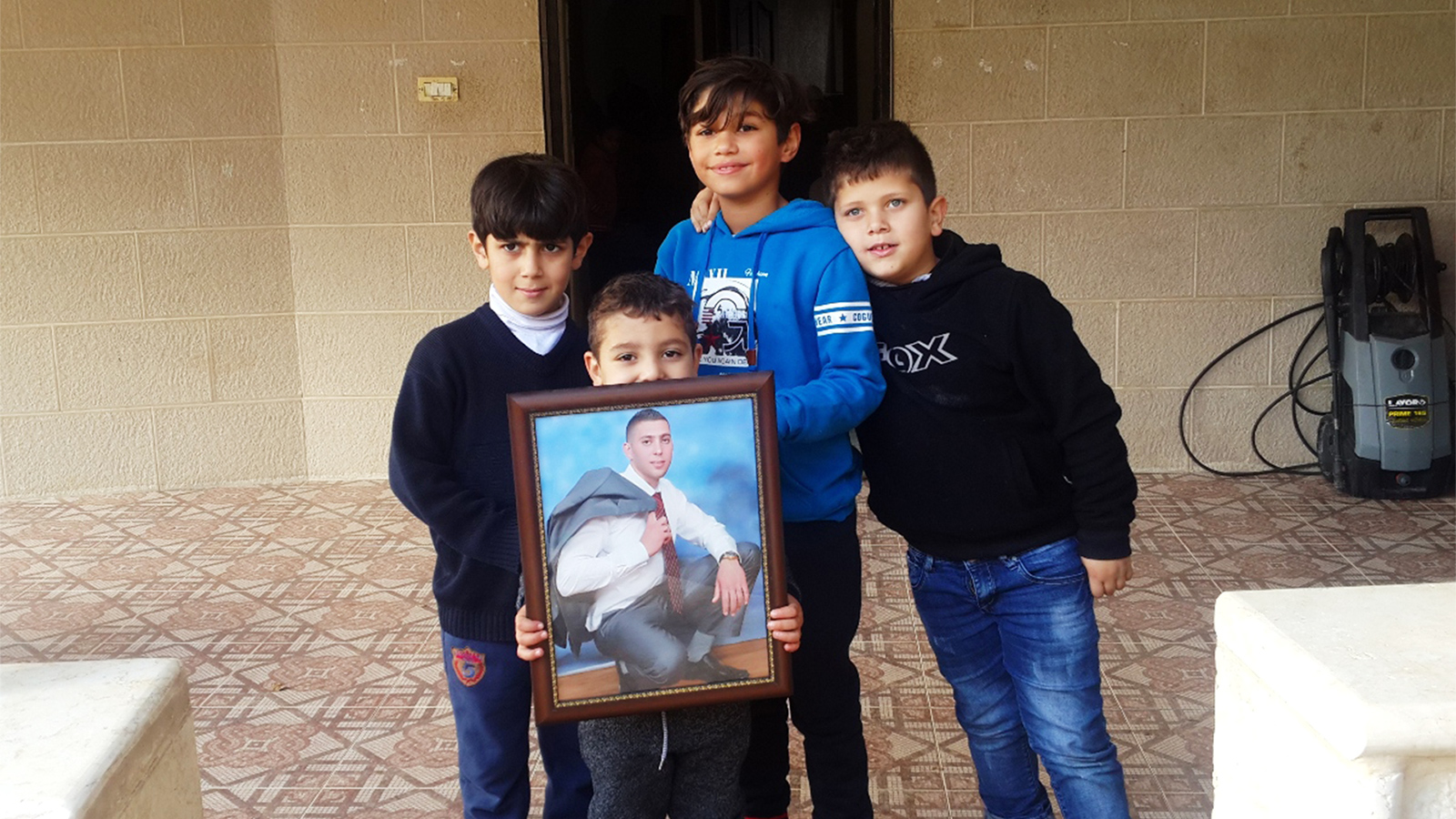 ‪قيس نجل الشهيد صالح البرغوثي يحمل صورة والده ويتوسط أقرانه بعد اغتيال والده مساء الأربعاء‬ (الجزيرة)