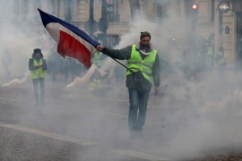 Yellow vests protest in Paris- - PARIS, FRANCE - DECEMBER 08: A yellow vests (Gilets jaunes) protester stands with French flag among smoke as French police use tear gas during demonstration against rising oil prices and deteriorating economic conditions in Paris, France on December 08, 2018.