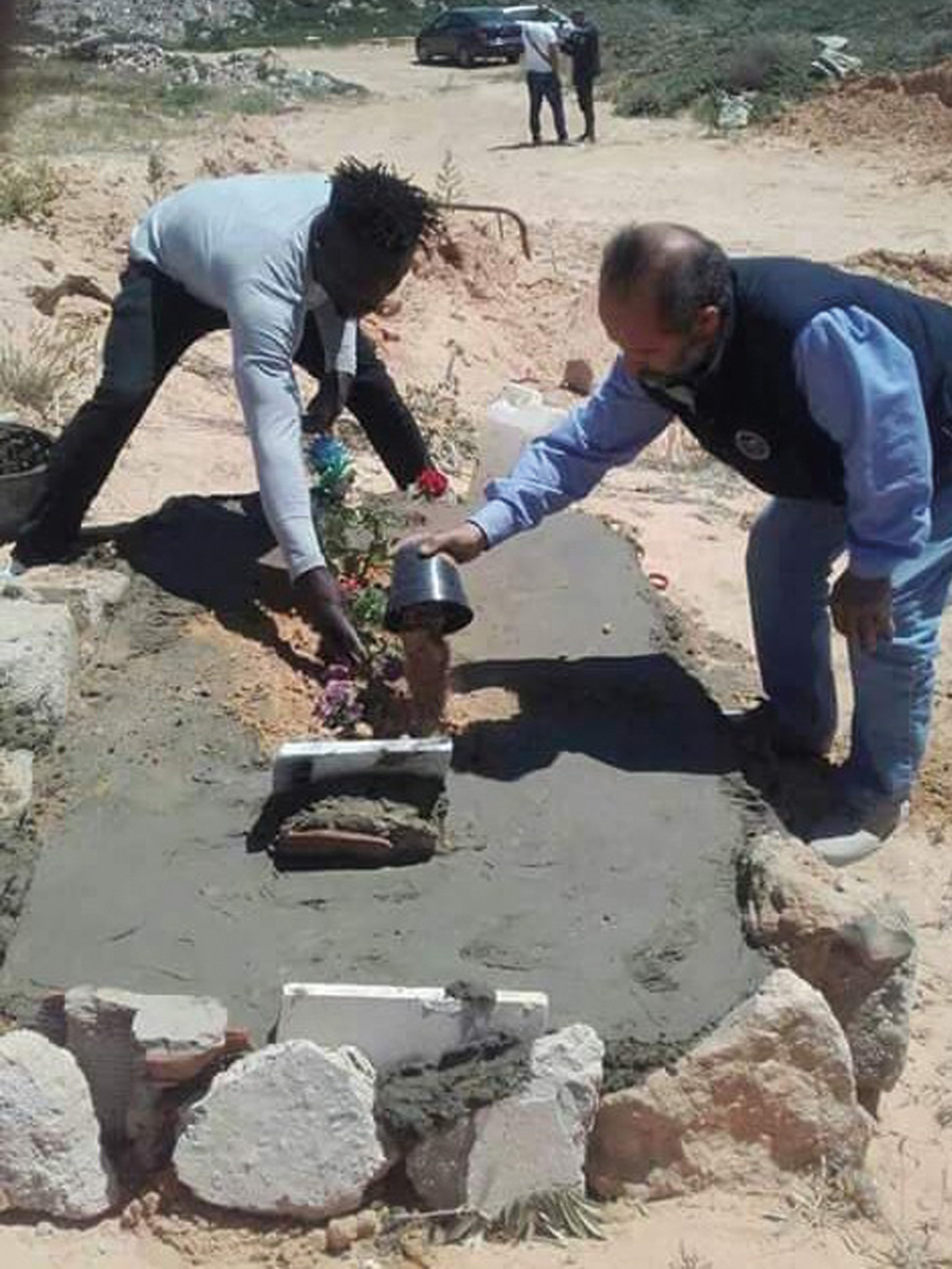 شمس الدين بصدد زراعة ورود على قبر برفقة أحد الأفارقة المهاجرين(الجزيرة نت)
