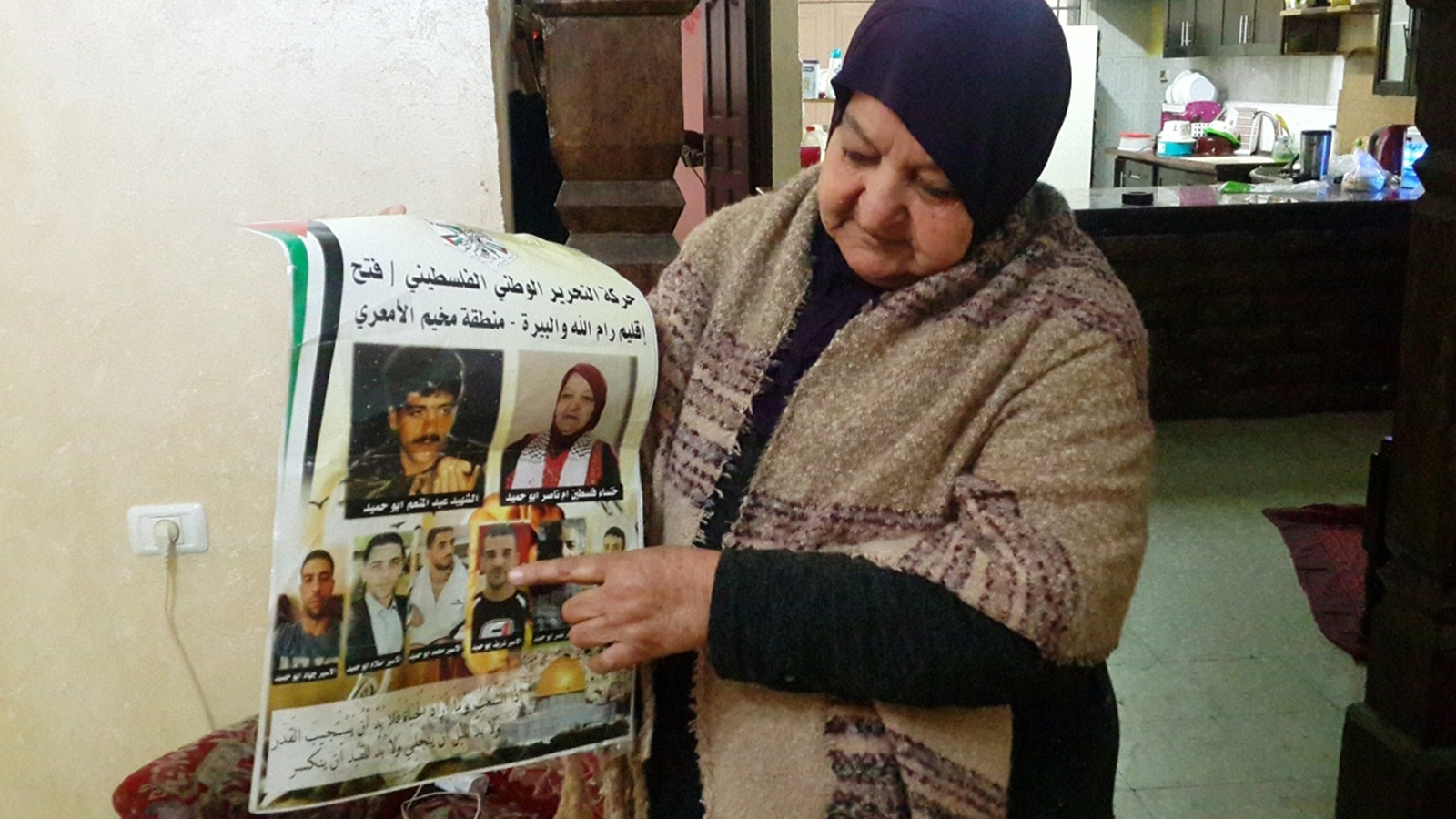 ‪لطيفة أبو حميد تحمل صور أبنائها المعتقلين في سجون الاحتلال قبل تدمير منزلها للمرة الثالثة‬ (الجزيرة)