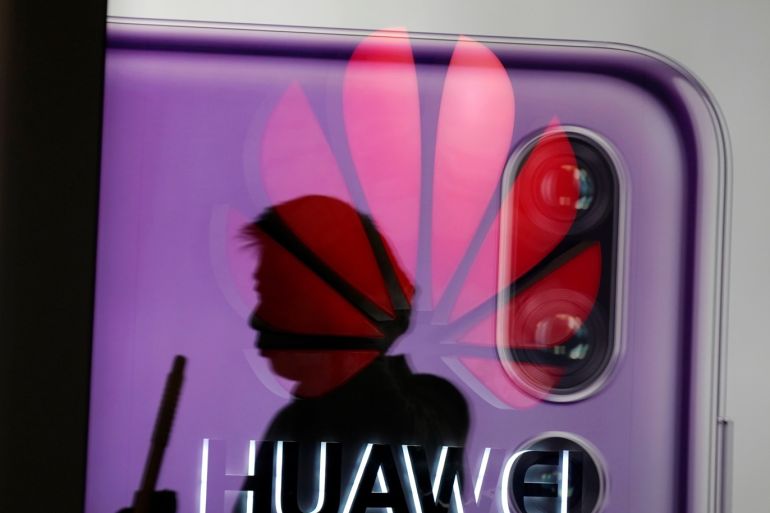 A man walking past a Huawei P20 smartphone advertisement is reflected in a glass door in front of a Huawei logo, at a shopping mall in Shanghai, China December 6, 2018. REUTERS/Aly Song