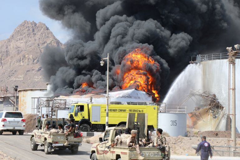 Soldiers ride on patrol trucks driving past an oil storage tank engulfed by fire at the Aden oil refinery one day after an explosion in the refinery in Aden, Yemen January 12, 2019. REUTERS/Fawaz Salman