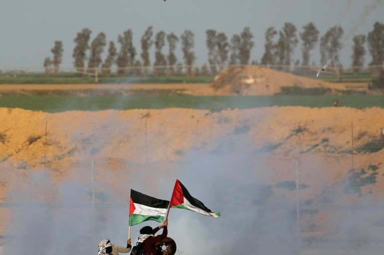 Women hold Palestinian flags as tear gas canisters are by fired by Israeli forces during a protest at the Israel-Gaza border fence, in the southern Gaza Strip February 8, 2019. REUTERS/Ibraheem Abu Mustafa