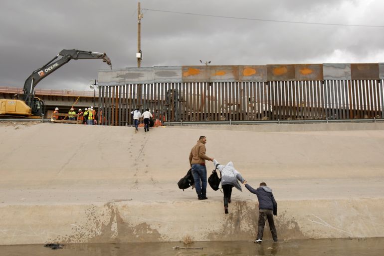 Migrants cross a river next to an excavator working in a section of the new wall between El Paso, Texas, in the United States and Ciudad Juarez as seen from the Mexican side of the border in Ciudad Juarez, Mexico, February 5, 2019. REUTERS/Jose Luis Gonzalezz