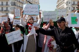 A police officer directs traffic while demonstrators carry signs as teachers and students take part in a protest demanding immediate political change in Algiers, Algeria March 13, 2019. The signs read: