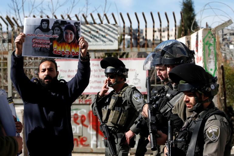A demonstrator holds a poster of jailed Palestinian as he stands next to Israeli border policemen during a protest in the West Bank city of Bethlehem January 9, 2018. REUTERS/Mussa Qawasma