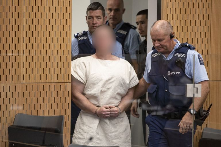 CHRISTCHURCH, NEW ZEALAND - MARCH 16: (EDITOR'S NOTE: Parts of this image have been pixelated at source to conceal the identity of the defendant due to court order.) The man charged in relation to the Christchurch massacre, Brenton Tarrant, is led into the dock for his appearance for murder in the Christchurch District Court on March 16, 2019 in Christchurch, New Zealand. At least 49 people are confirmed dead, with more than 40 people injured following attacks on two m