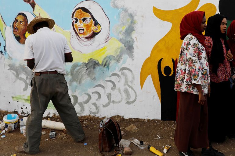 A Sudanese protester paints a mural as a group of demonstrators stand next to him in Khartoum, Sudan April 14, 2019. REUTERS/Umit Bektas