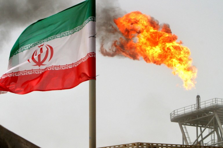A gas flare on an oil production platform in the Soroush oil fields is seen alongside an Iranian flag in the Persian Gulf, Iran, July 25, 2005.    REUTERS/Raheb Homavandi/File Photo
