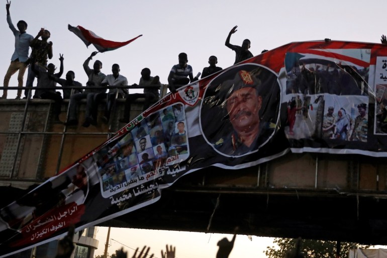 Protesters tear down a banner with a picture of Sudan's head of transitional council, Lieutenant General Abdel Fattah Al-Burhan Abdelrahman and pictures of Sudanese soldiers and protesters together, minutes after it was hanged to a railroad bridge near the Defence Ministry in Khartoum, Sudan, April 20, 2019. REUTERS/Umit Bektas