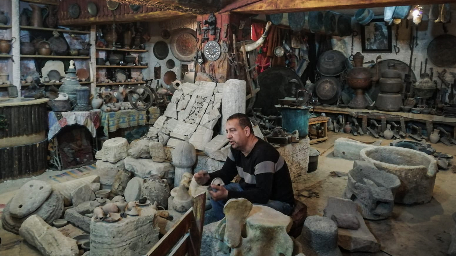  مروان شهوان يجلس بين آثار جمعها على امتداد 35 عاما  (الجزيرة)