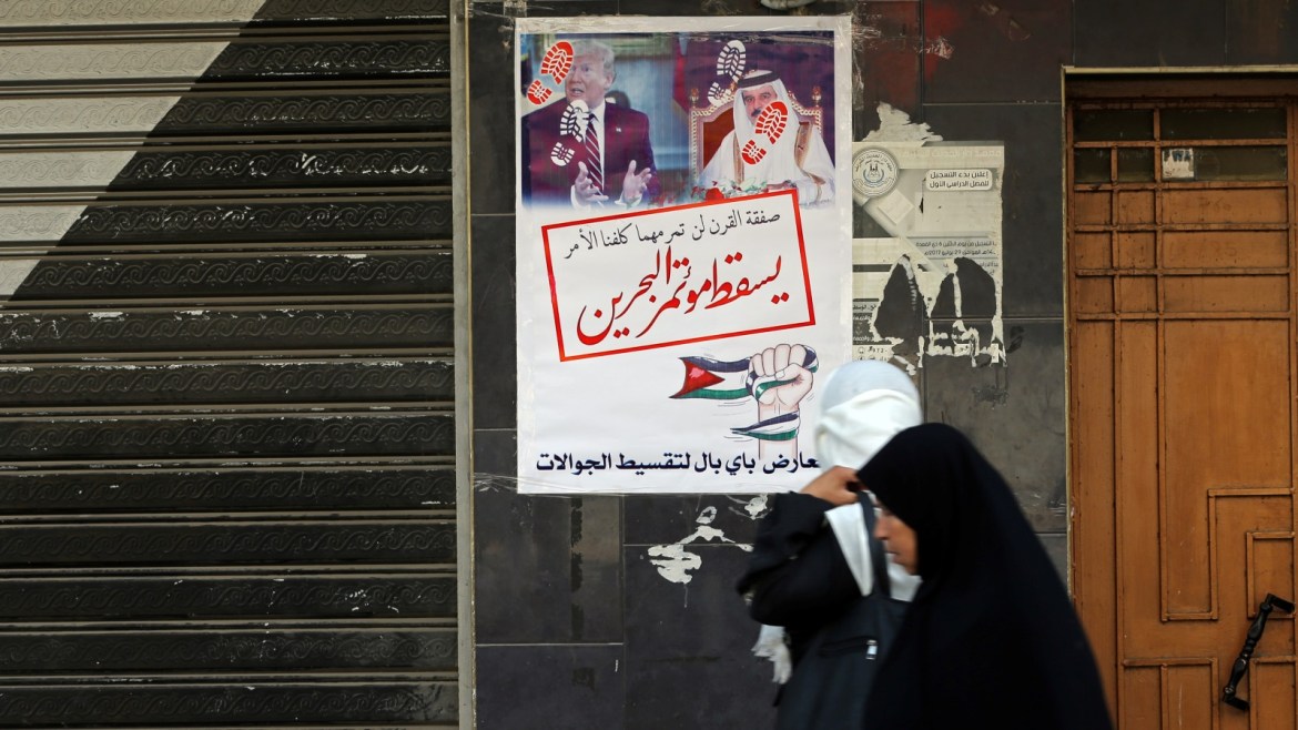 Women walk past banners showing pictures of Bahrain's King Hamad bin Isa Al Khalifa and U.S. President Donald Trump and reading