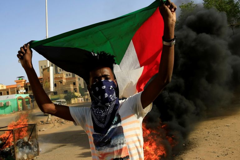 A protester carries a Sudanese national flag as he burns tyres during a demonstration against a report of the Attorney-General on the dissolution of the sit-in protest in Khartoum, Sudan July 27, 2019. REUTERS/Mohamed Nureldin Abdallah