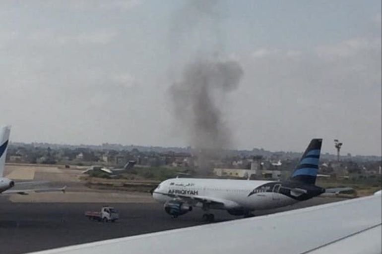 أعمدة الدخان تتصاعد خلف إحدى الطائرات الرابضة على مدرج مطار معيتيقة الدولي شرقي طرابلس