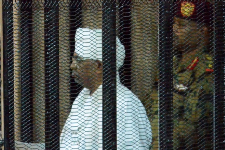 epa07780604 Sudan's ousted president Omar Hassan al-Bashir (L) stands in a cage during his trial at a courtroom in Khartoum, Sudan, 19 August 2019. Al-Bashir was ousted on 11 April after months of protests and some 30 years in power. According to local media reports, al-Bashir returned to court on 19 August to answer for corruption charges. The trial resumed two days after the military council and the opposition signed a power sharing deal, hoping to end months of cris