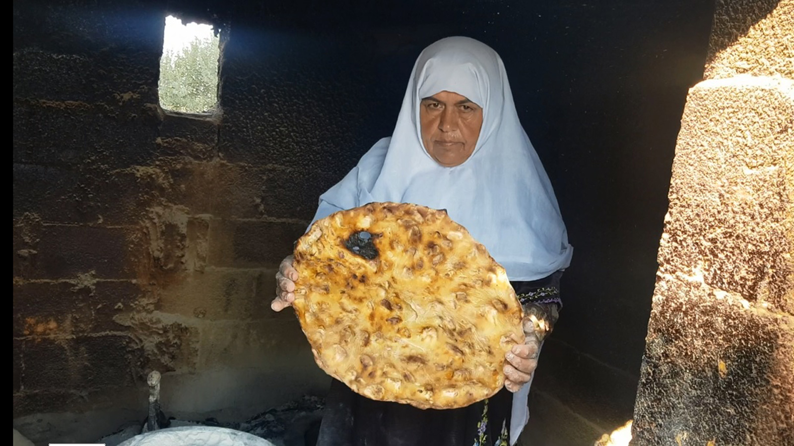 ‪أم عبد الله تحمل رغيف خبز  طابون من القطع الكبير من إنتاجها‬ (الجزيرة)