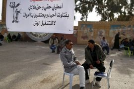 Unemployed people sit at a cafe next to a sign in Kasserine, where young people have been demonstrating for jobs since last week, January 30, 2016. The sign reads: