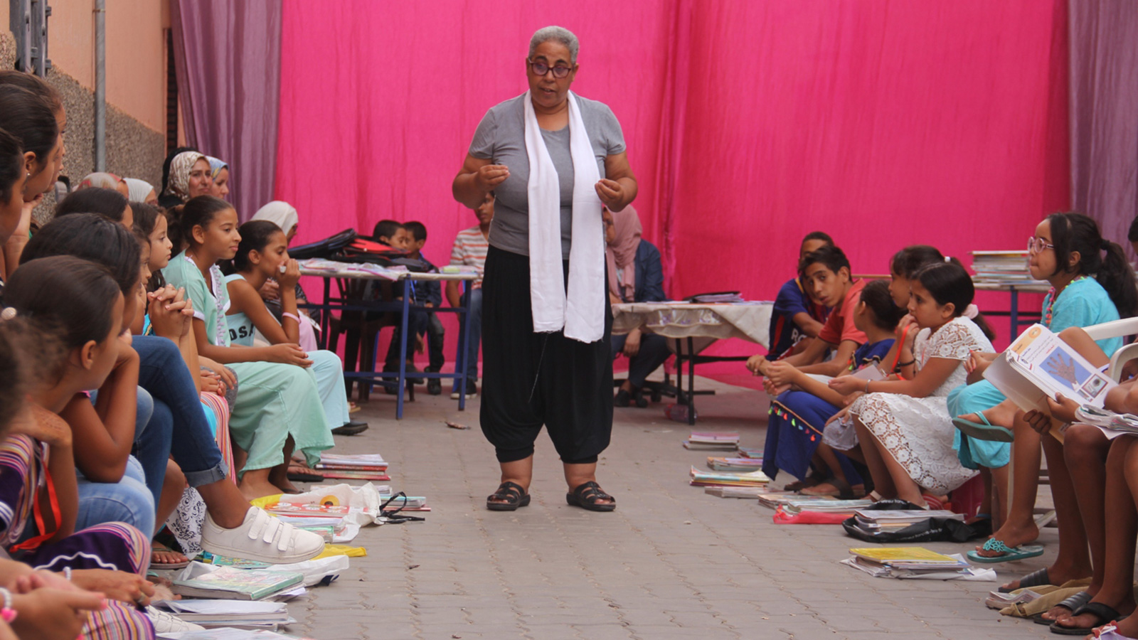 ‪الفنانة حياة غافري تشرح للأطفال مبادرتها حول إحياء دلالة الكتب أمام منزلها بحي الداوديات‬ (الجزيرة)