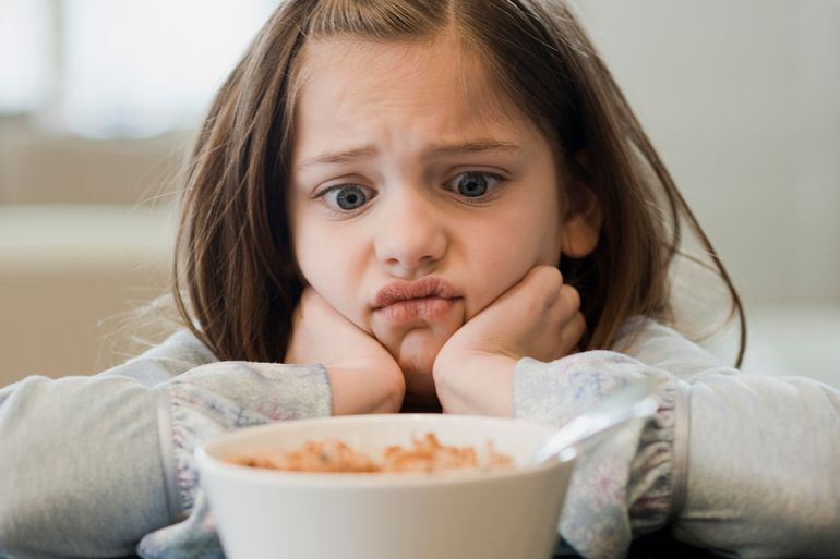 تناول الطعام -Displeased girl looking at bowl of cereal