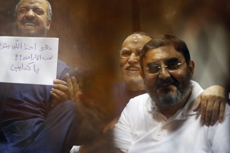 Muslim Brotherhood's senior member Mohamed El-Beltagy (L) smiles as he holds up a sheet of paper that reads "You liars, we did not steal the land" next to Essam Al-Haddad (R), former head of the Office of the Ousted Egyptian president Mohamed Mursi, in the defendant's cage during their trial with other leaders of the Muslim Brotherhood on charges of spying and terrorism at a court in the police academy on the outskirts of Cairo, November 18, 2014. REUTERS/Amr Abdallah Dalsh (EGYPT - Tags: POLITICS CRIME LAW CIVIL UNREST)