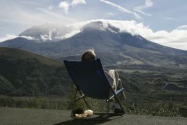 A tourist to the Cold Lake Visitor Center relaxes in the afternoon sun while watching Mount St. Helens October 7, 2004. Government scientists have reduced the eruption threat level from three to two though seismic activity has begun to rise again inside the volcano. REUTERS/Andy Clark NO RIGHTS CLEARANCES OR PERMISSIONS ARE REQUIRED FOR THIS IMAGE AC/SV