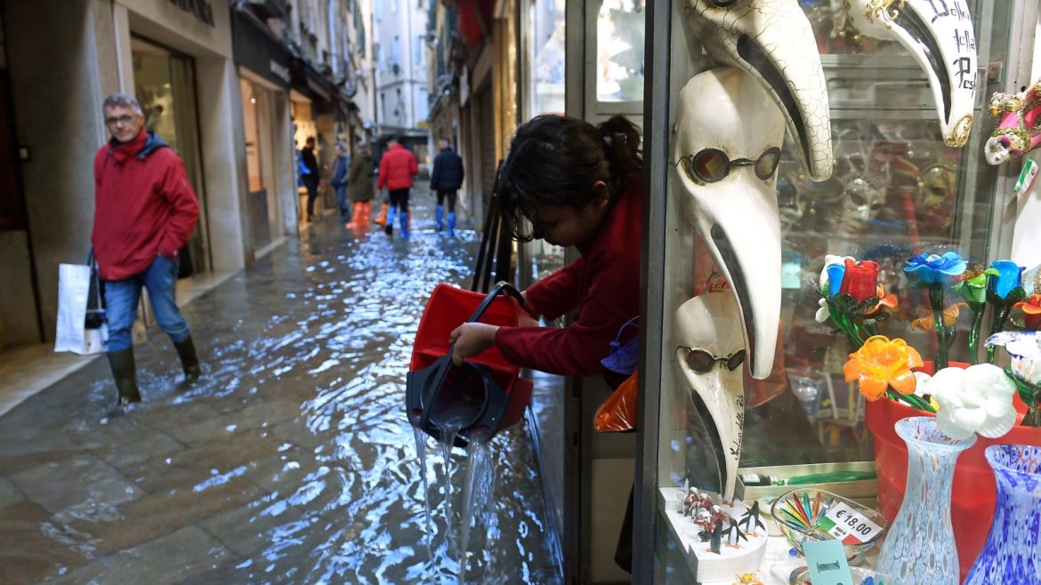 A woman pours out water from a shop onto a flooded walkway during a period of seasonal high water in Venice, Italy, November 14, 2019. REUTERS/Flavio Lo Scalzo