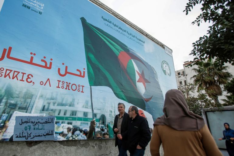 People walk past a campaign poster for presidential election in Algiers, Algeria November 2, 2019. The poster reads: