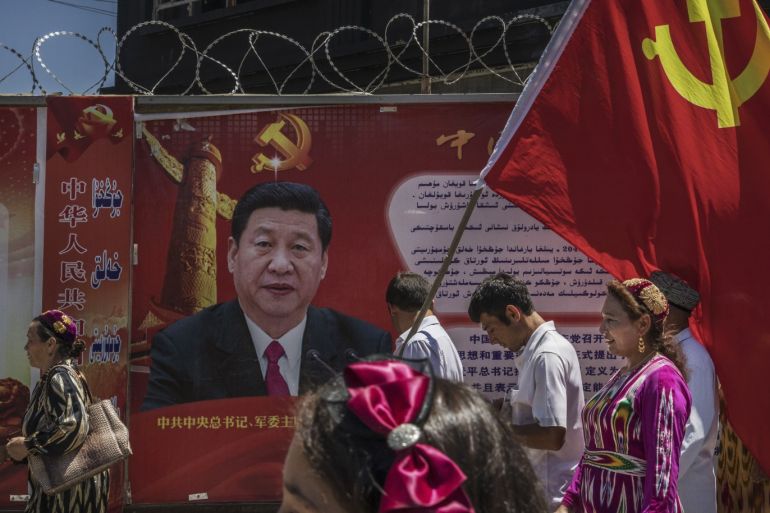 KASHGAR, CHINA - JUNE 30: Ethnic Uyghur members of the Communist Party of China carry a flag past a billboard of Chinese President Xi Jinping as they take part in an organized tour on June 30, 2017 in the old town of Kashgar, in the far western Xinjiang province, China. Kashgar has long been considered the cultural heart of Xinjiang for the province's nearly 10 million Muslim Uyghurs. At an historic crossroads linking China to Asia, the Middle East, and Europe, the ci