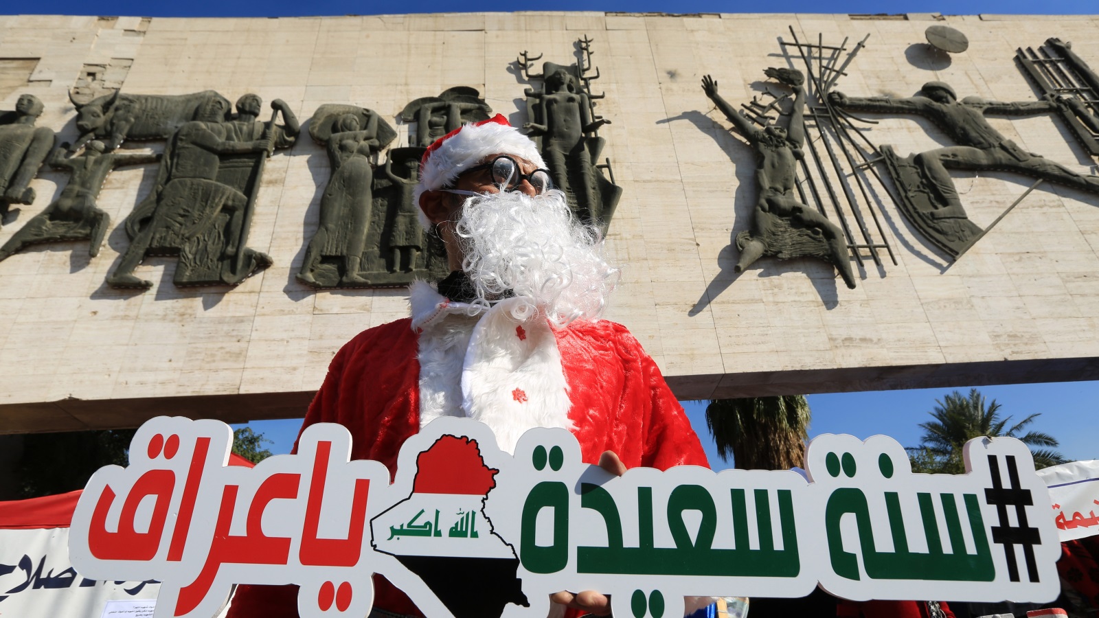 ناشط يرتدي ملابس بابا نويل ويحمل لوحة في ساحة التحرير يتمنى سنة سعيدة للعراق في 2020 (الأناضول)