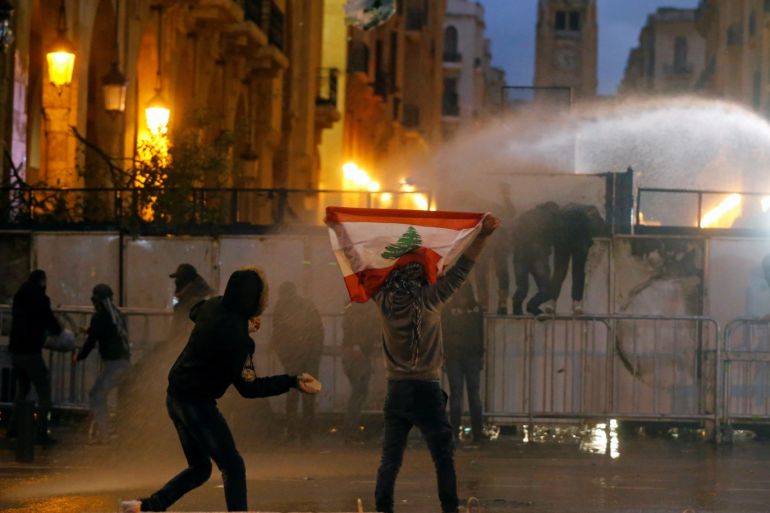 A demonstrator holds up a national flag as police use water cannon during a protest against the newly formed government in Beirut, Lebanon January 22, 2020. REUTERS/Mohamed Azakir