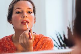 Woman applying lipstick in front of a big mirror.قواعد جمالية يجب على السيدة الملكيةالالتزام بها