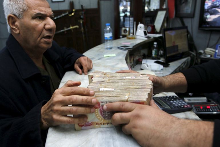 A man (L) changes Iraqi dinars to U.S. dollars at a currency exchange shop in Baghdad December 21, 2015. REUTERS/Khalid al Mousily