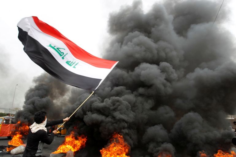 A demonstrator carries an Iraqi flag as he walks near burning tires blocking a road during ongoing anti-government protests, in Baghdad, Iraq January 19, 2020. REUTERS/Khalid al-Mousily