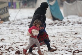 An internally displaced woman holds the hand of a child carrying bread, as they walk on snow at a makeshift camp in Azaz, Syria February 13, 2020. REUTERS/Khalil Ashawi