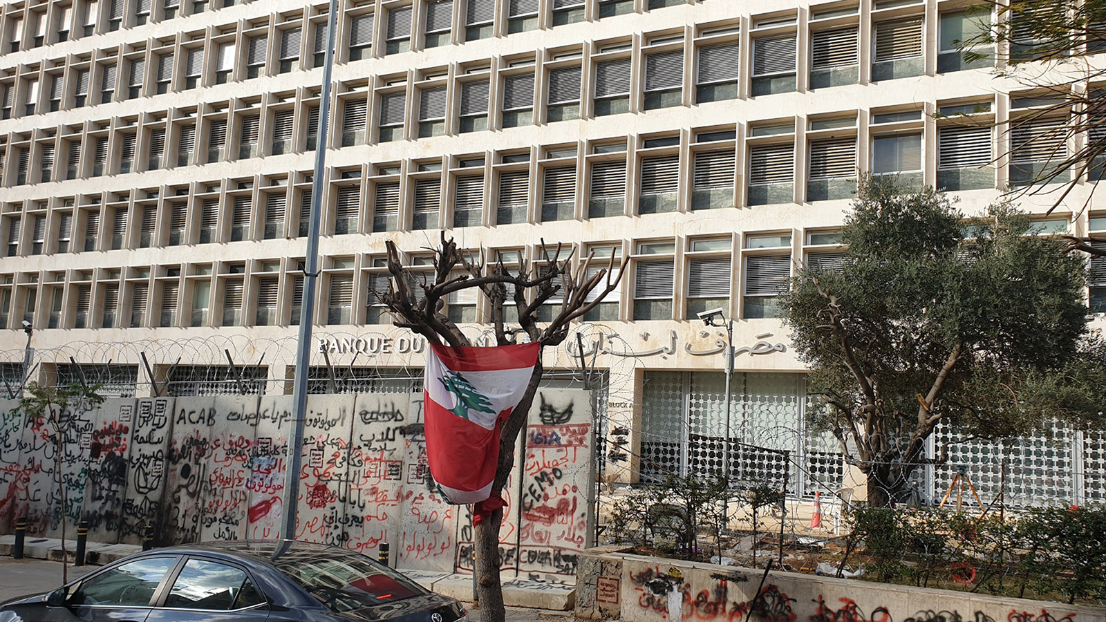 ‪مصرف لبنان الداعم لمؤسسة الإسكان وتبدو شعارات الثورة على الجدران الموضوعة حديثا لحمايته‬ (الجزيرة)