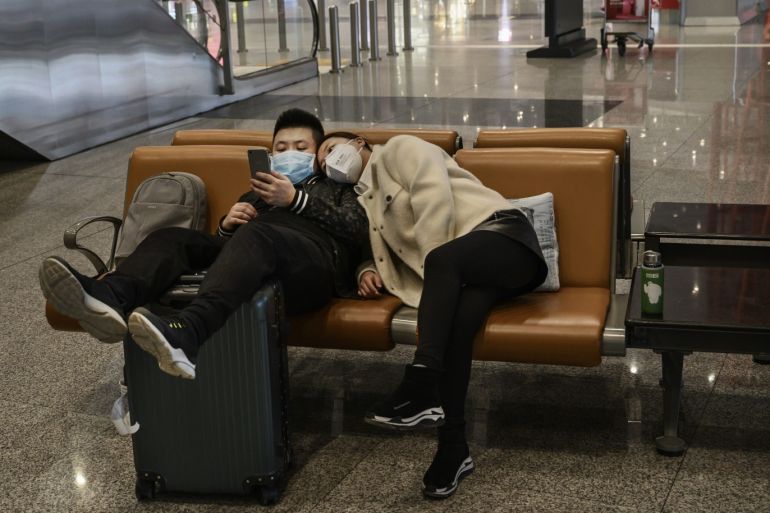 BEIJING, CHINA - MARCH 24: A Chinese couple wear protective masks as they watch a show on their mobile while waiting for a flight at Beijing Capital International Airport on March 24, 2020 in Beijing, China. In an effort to prevent imported cases of the virus, China's capital will enforce stronger restrictions on incoming arrivals as of midnight on March 25, 2020 and all international flights will be diverted to other cities in the country where passengers will be test