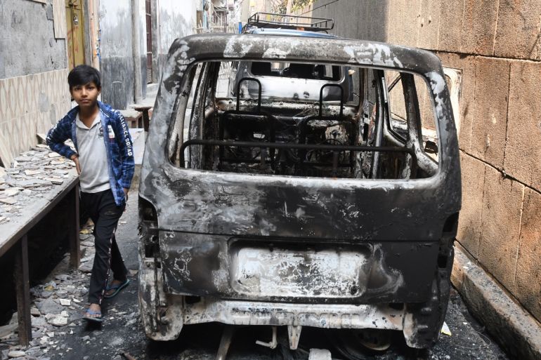 epa08258840 An Indian child passes near a burnt car on a street after the clashes that broke out in New Delhi, India, 29 February 2020. At least 42 people have been killed in the fighting that broke out between supporters and opponents of the...
