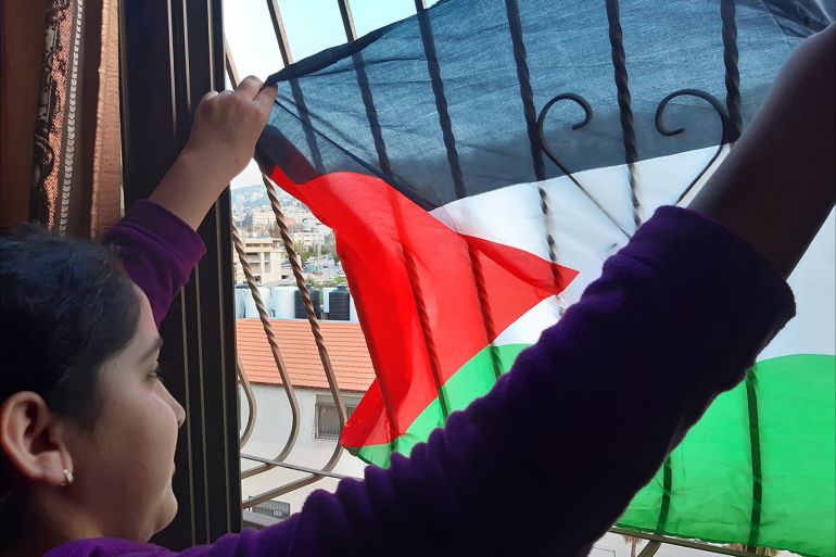 طفلة فلسطينية ترفع العلم الفلسطيني من شباك نافذة منزلهم بمدينة نابلس- الضفة الغربية
