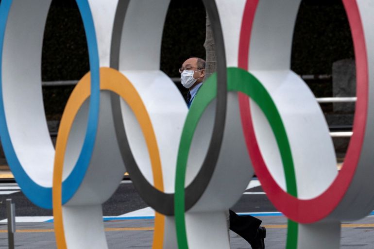 A man wearing a protective face mask, following an outbreak of the coronavirus disease (COVID-19), walks past the Olympic rings in front of the Japan Olympics Museum in Tokyo, Japan March 13, 2020. REUTERS/Athit Perawongmetha