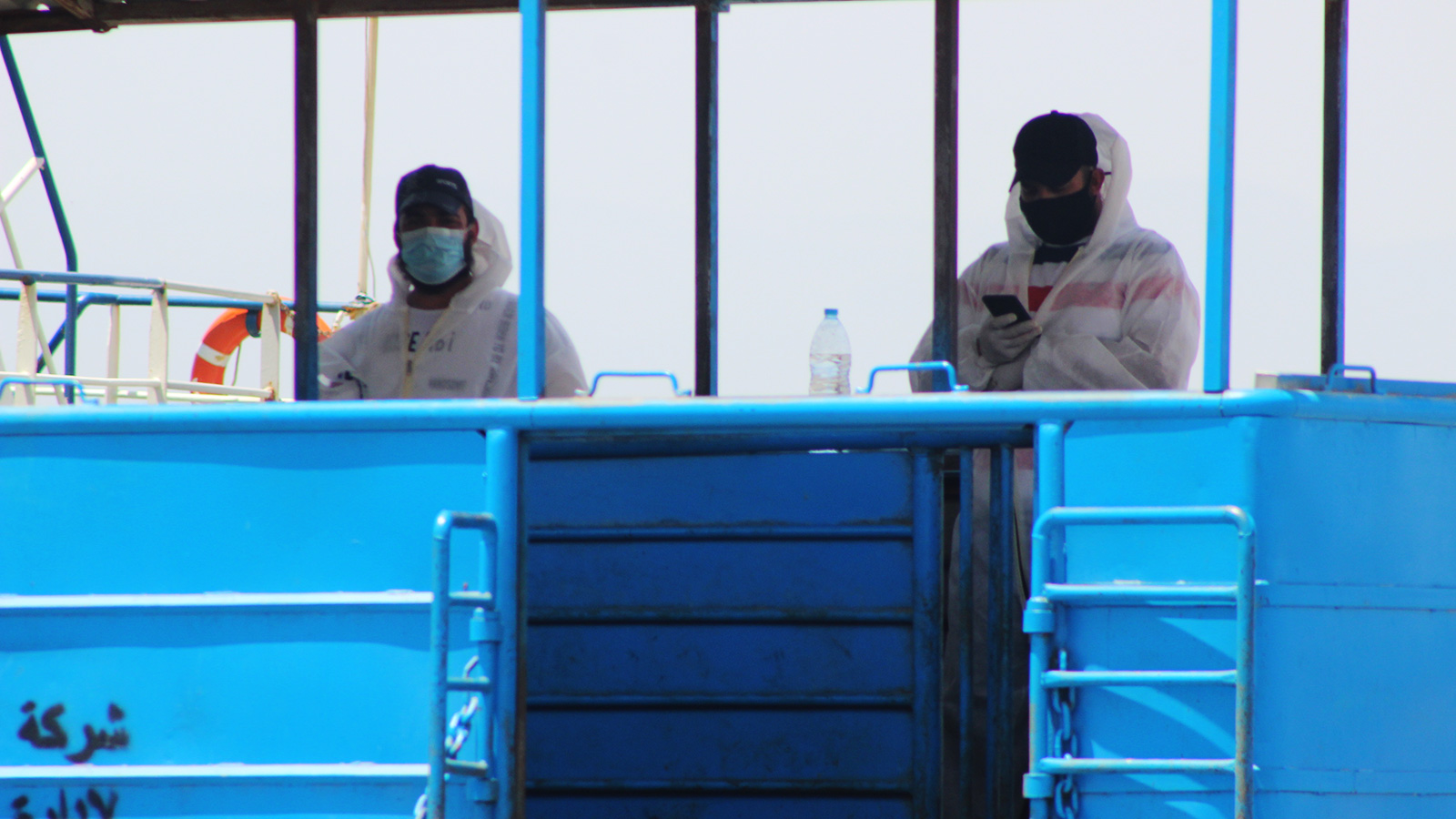 ‪عمال الموانئ يرتدون الواقيات الطبية لتعقيم البواخر البحرية القادمة بالبضائع المستوردة‬ (الجزيرة)