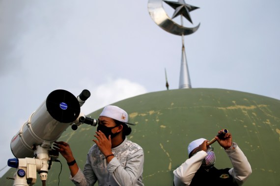 A boarding school student and an official wearing protective masks use a telescope and a monocular to view the moon on the roof of Al Musariin mosque to mark the first day of Ramadan, as the spread of the coronavirus disease (COVID-19) continues, in Jakarta, Indonesia, April 23, 2020. REUTERS/Willy Kurniawan REFILE - CORRECTING ID TPX IMAGES OF THE DAY