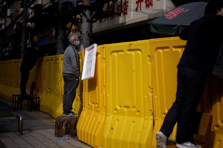 Residents wearing face masks pay for groceries by standing on chairs to peer over barriers set up to ring fence a wet market on a street in Wuhan, Hubei province, the epicentre of China's coronavirus disease (COVID-19) outbreak, April 1, 2020. REUTERS/Aly Song